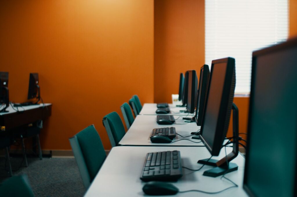 Courses Modern computers with keyboards and mice placed in row on table with chairs in contemporary workplace with orange walls